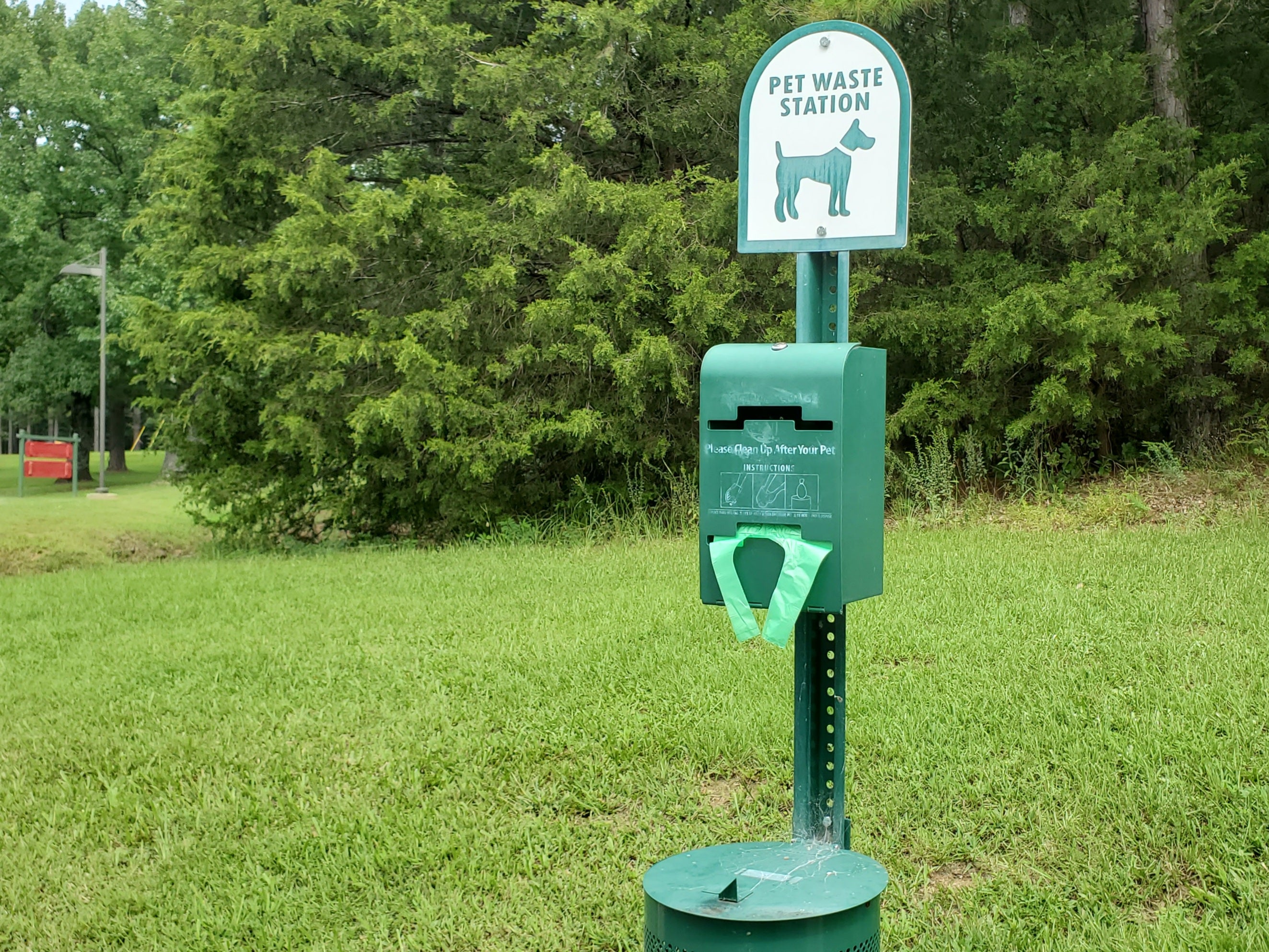 A green and white sign with a drawing of a dog, and the words “Pet Waste Station” with a bag dispenser and trash can